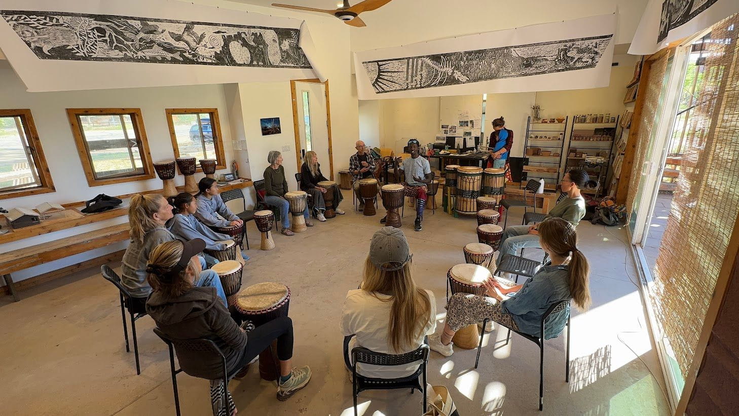People sitting in a circle playing djembe drums in a workshop.