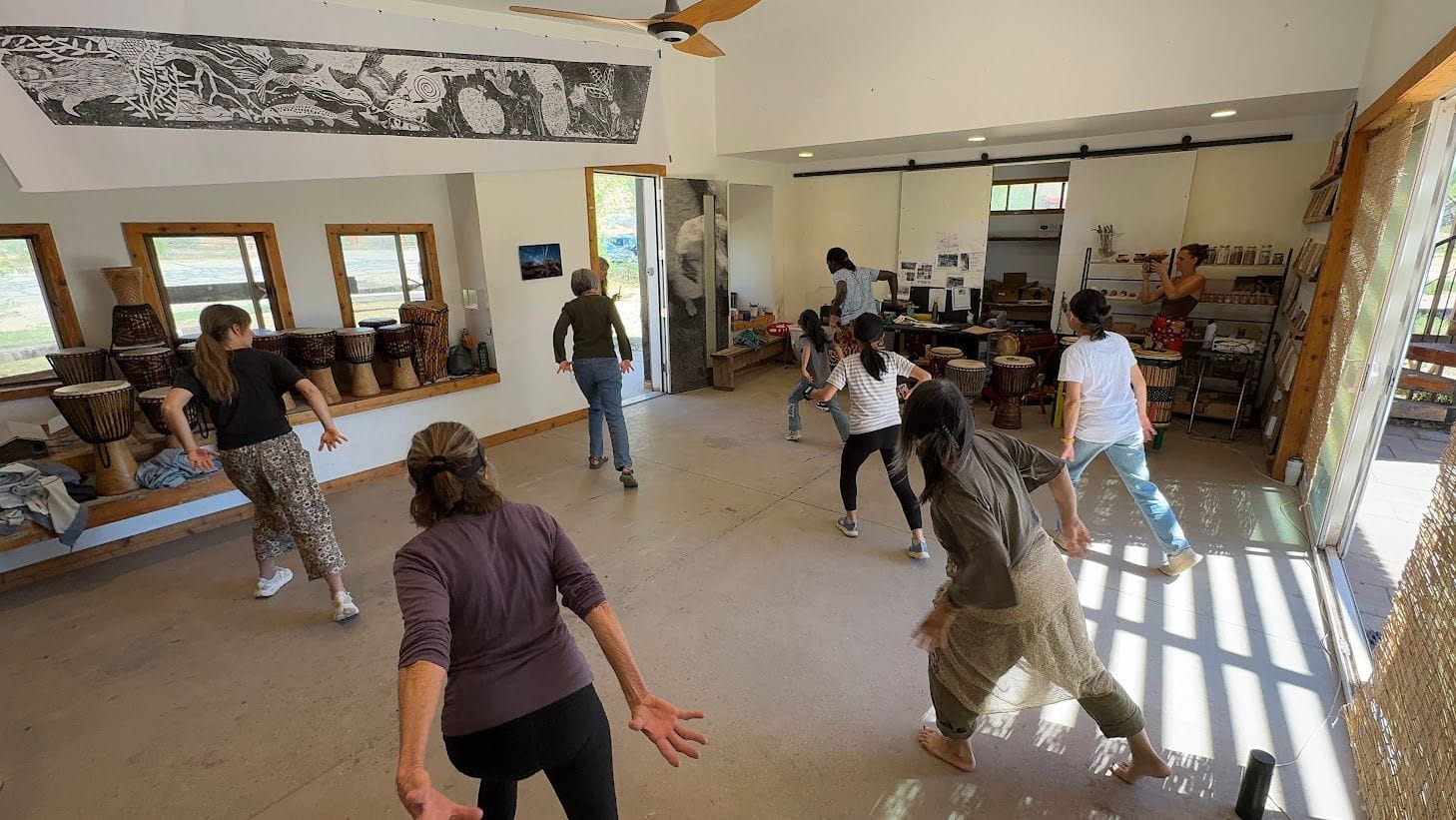 People dancing in a studio with drums and artwork.