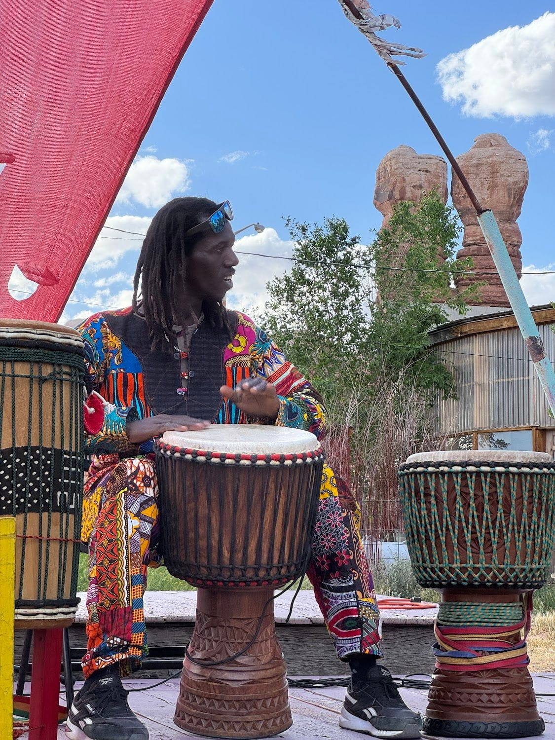 Man with dreadlocks playing djembe drums outdoors.