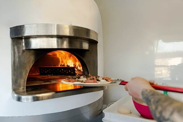A person putting pizza into a fire oven AI-generated content may be incorrect.