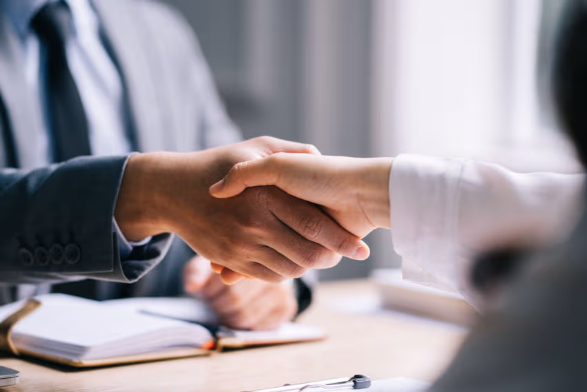 Two people shake hands across a desk