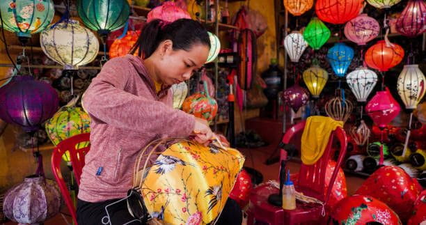 Vietnamese woman making traditional lanterns in Hoi An city, Vietnam Vietnamese woman making traditional silk hanging lanterns, night market in Hoi An. Hoi An is situated on the east coast of Vietnam. Its old town is a UNESCO World Heritage Site because of its historical buildings. 8 Best Things to Buy in Vietnam stock pictures, royalty-free photos & images