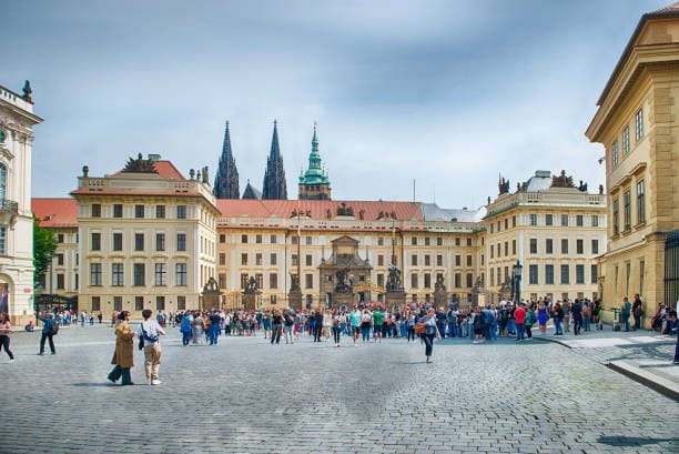 Tourists entering Prague Castle complex with st. Vitus Cathedral PRAGUE - MAY 11, 2024: Tourists walking towards the entrance of Prague Castle complex with st. Vitus Cathedral towering in the background on a cloudy summer day Places to Visit in the Czech Republic stock pictures, royalty-free photos & images