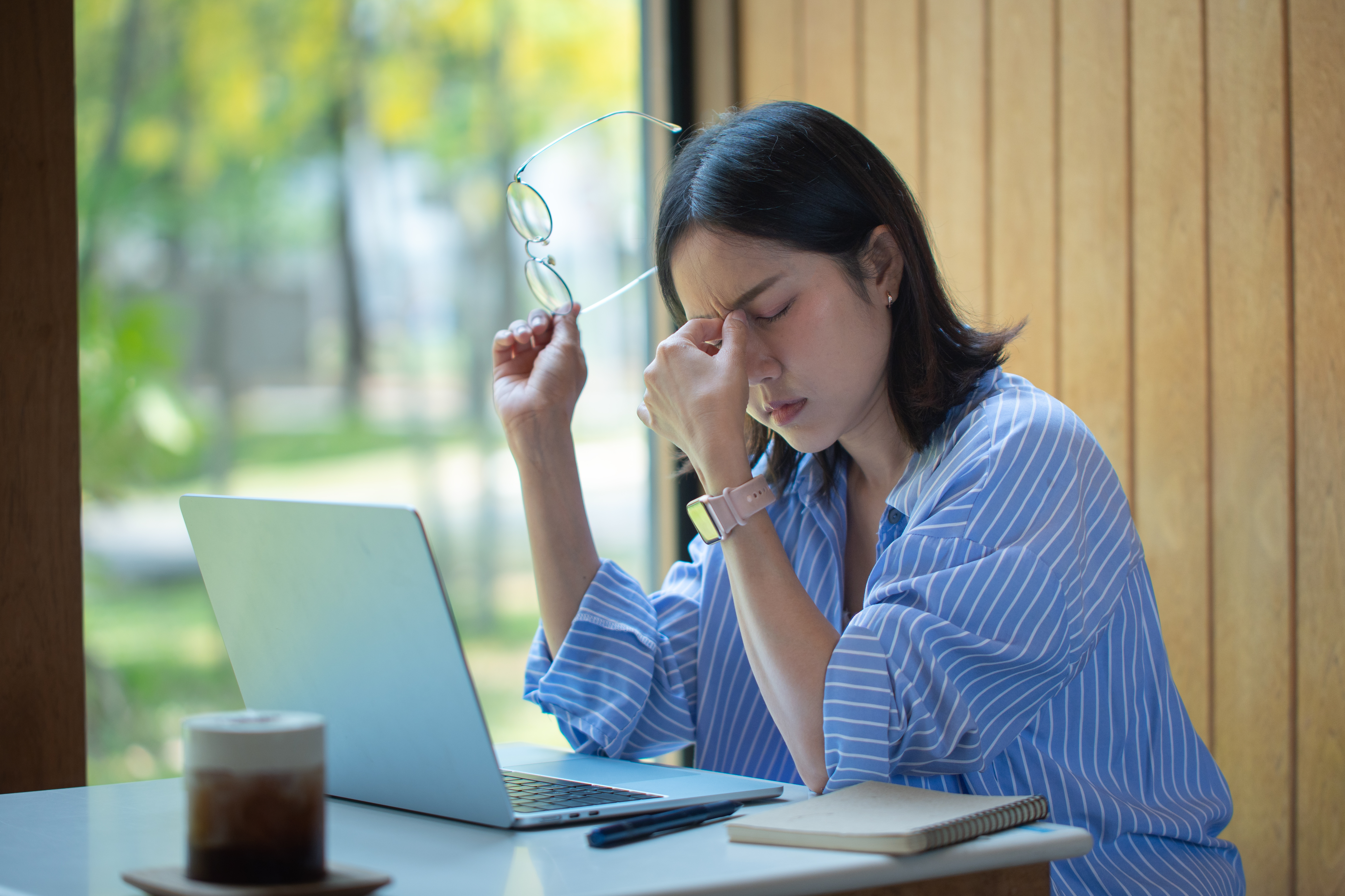 A woman in a blue striped shirt sits at a desk with a laptop.
