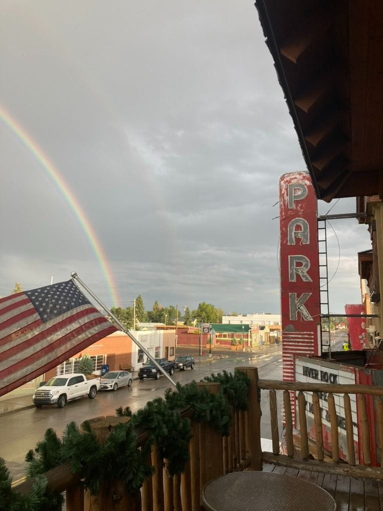 Downtown Walden as seen from the Antlers Inn Balcony. A recent rainstorm has cast a rainbow in the distance against dark stormy summer skies. The American flag flies in the foreground and the old Park Theatre sign sits proudly with recent summer events on the marquee.
