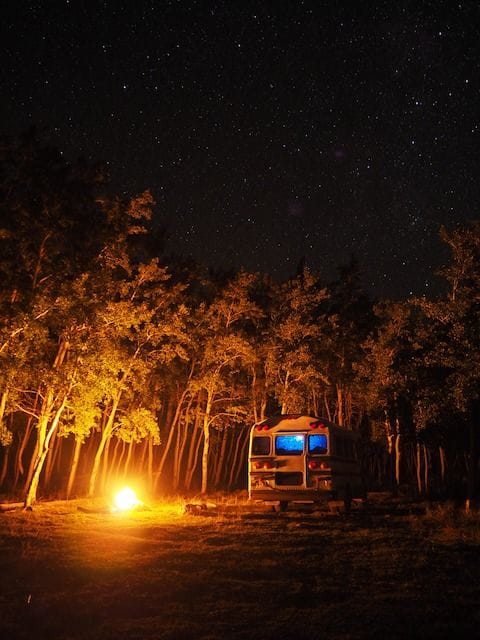 A converted school bus boondocker, also known as a "skoolie" parked near a campfire under starlight.