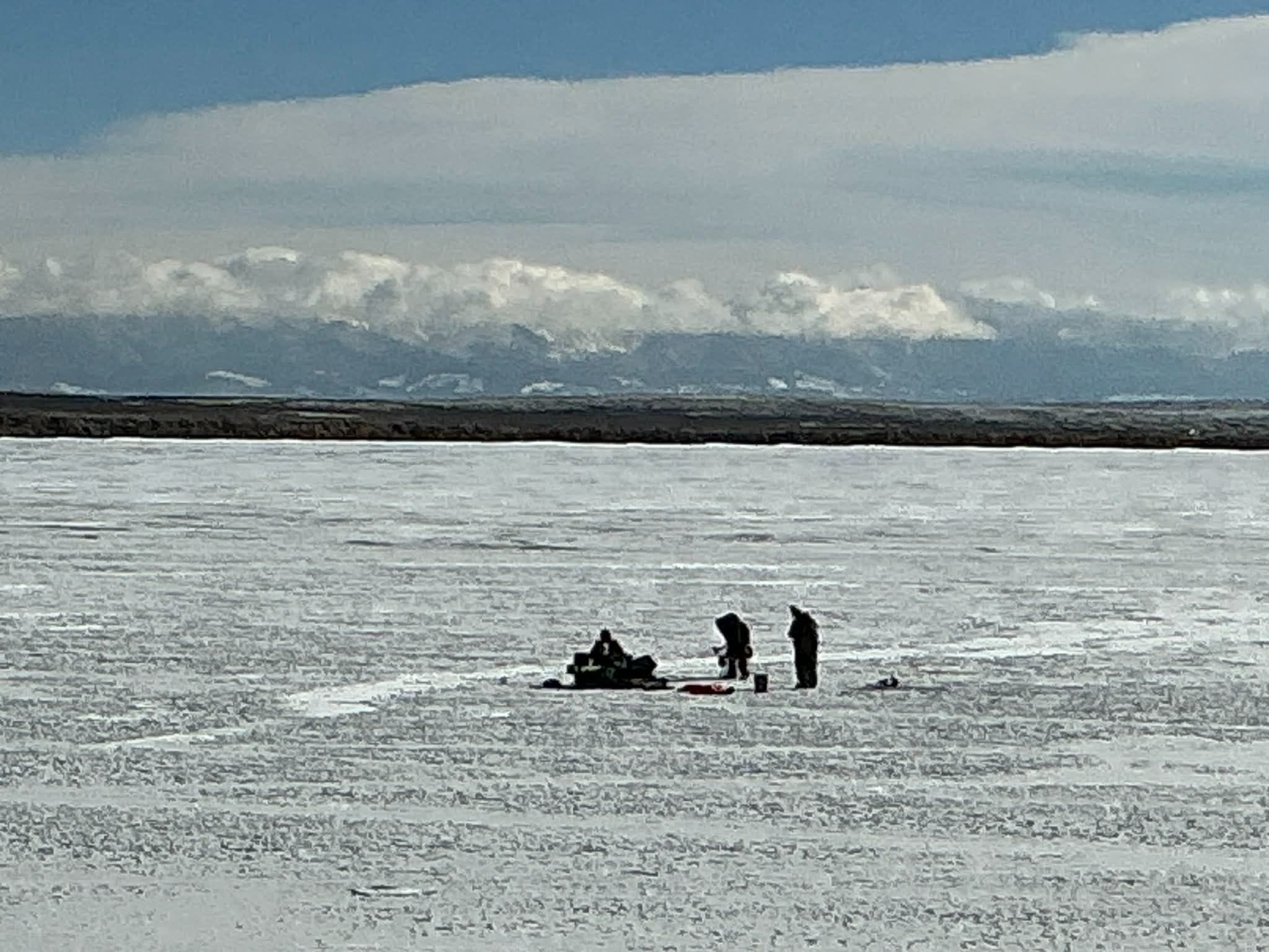 Ice anglers out on a frozen Lake John. Snowy mountains in the distance and blue skies above