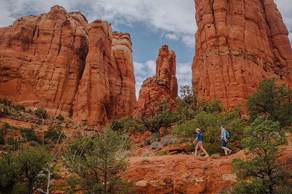 Woman and man walk across a red rock landscape