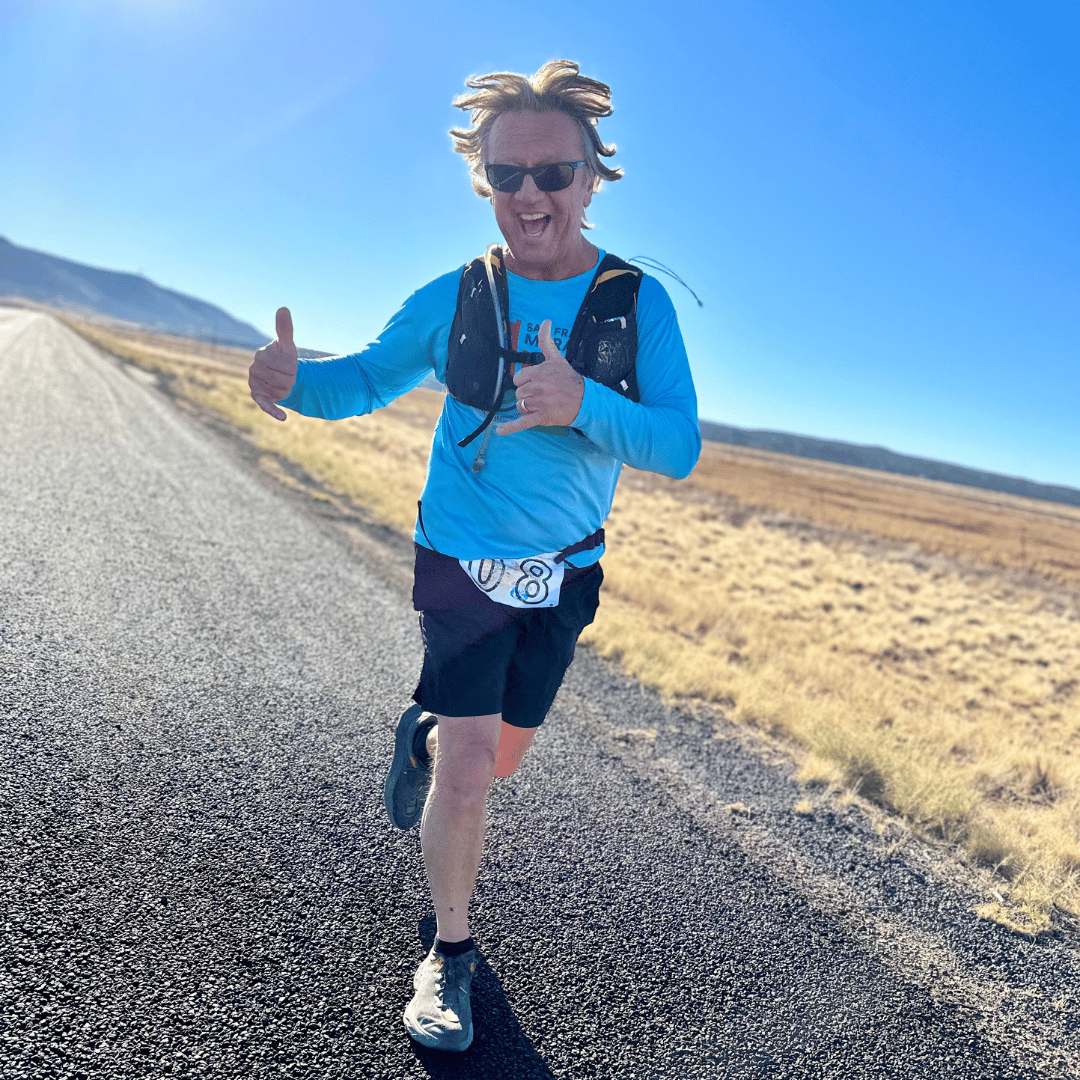 man running along the road giving a thumbs up