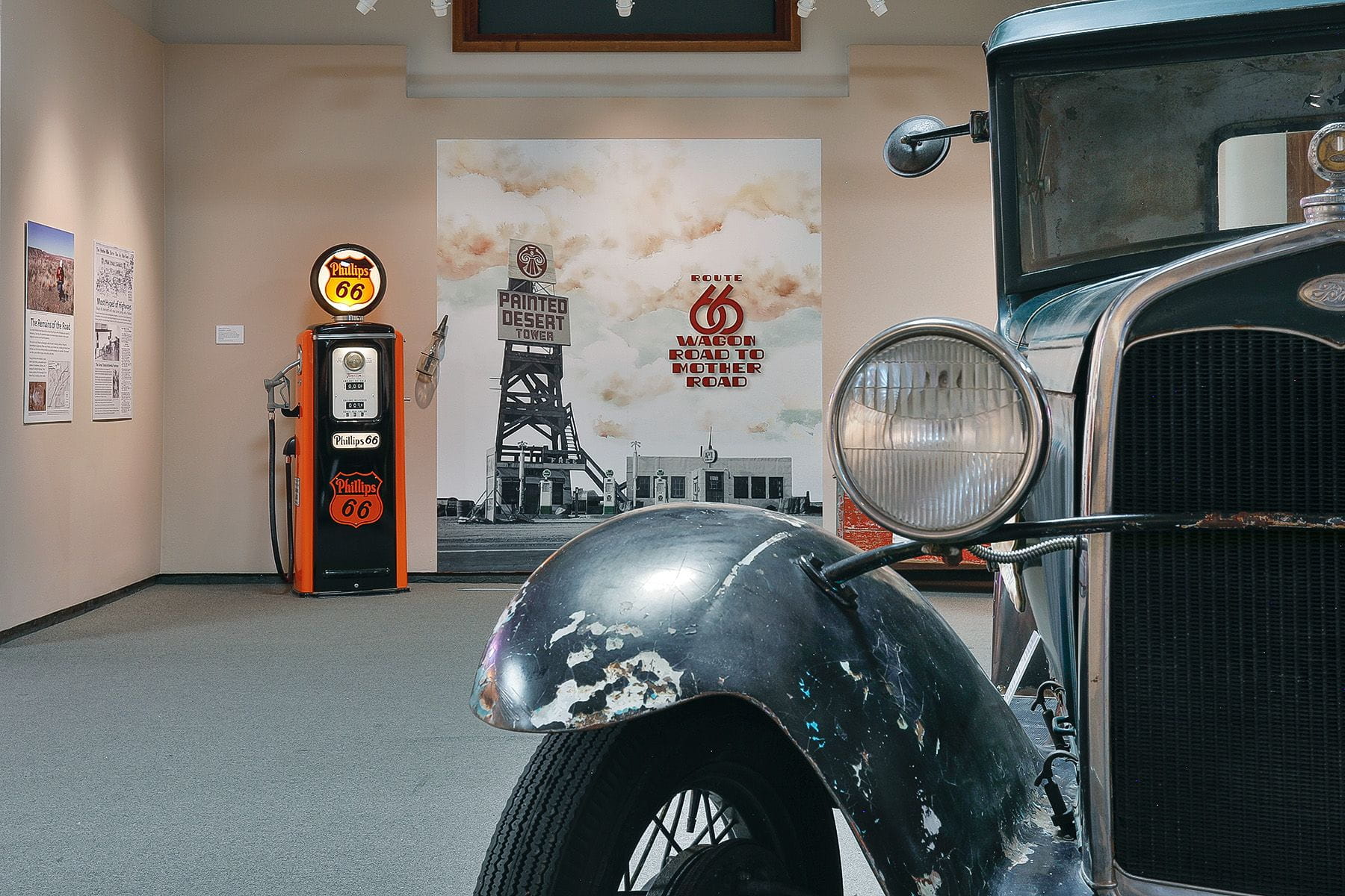 a corner of an antique vehicle inside a museum exhibit. A vintage gas pump in the background.