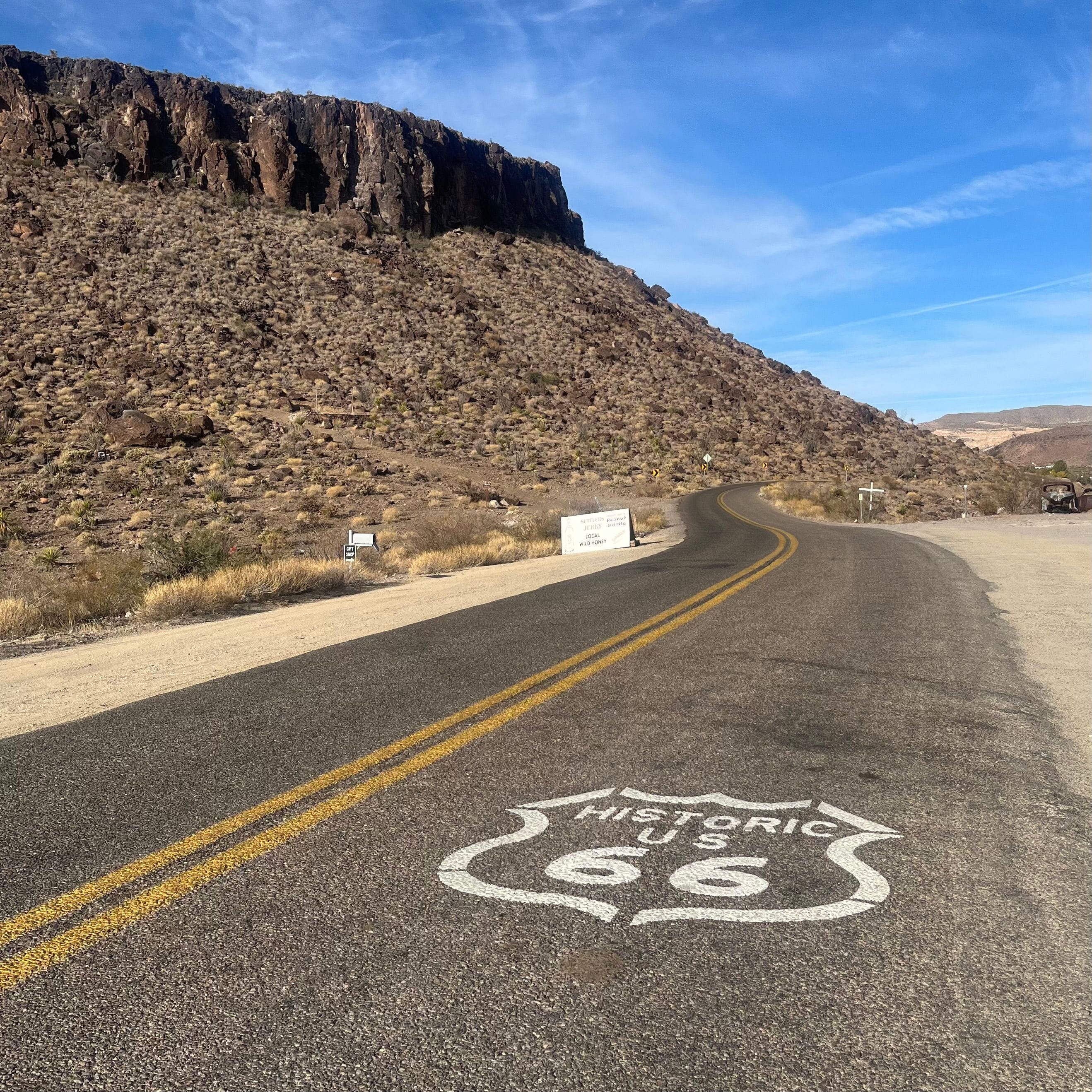 road with white route 66 shield painted on it. mountain in the background