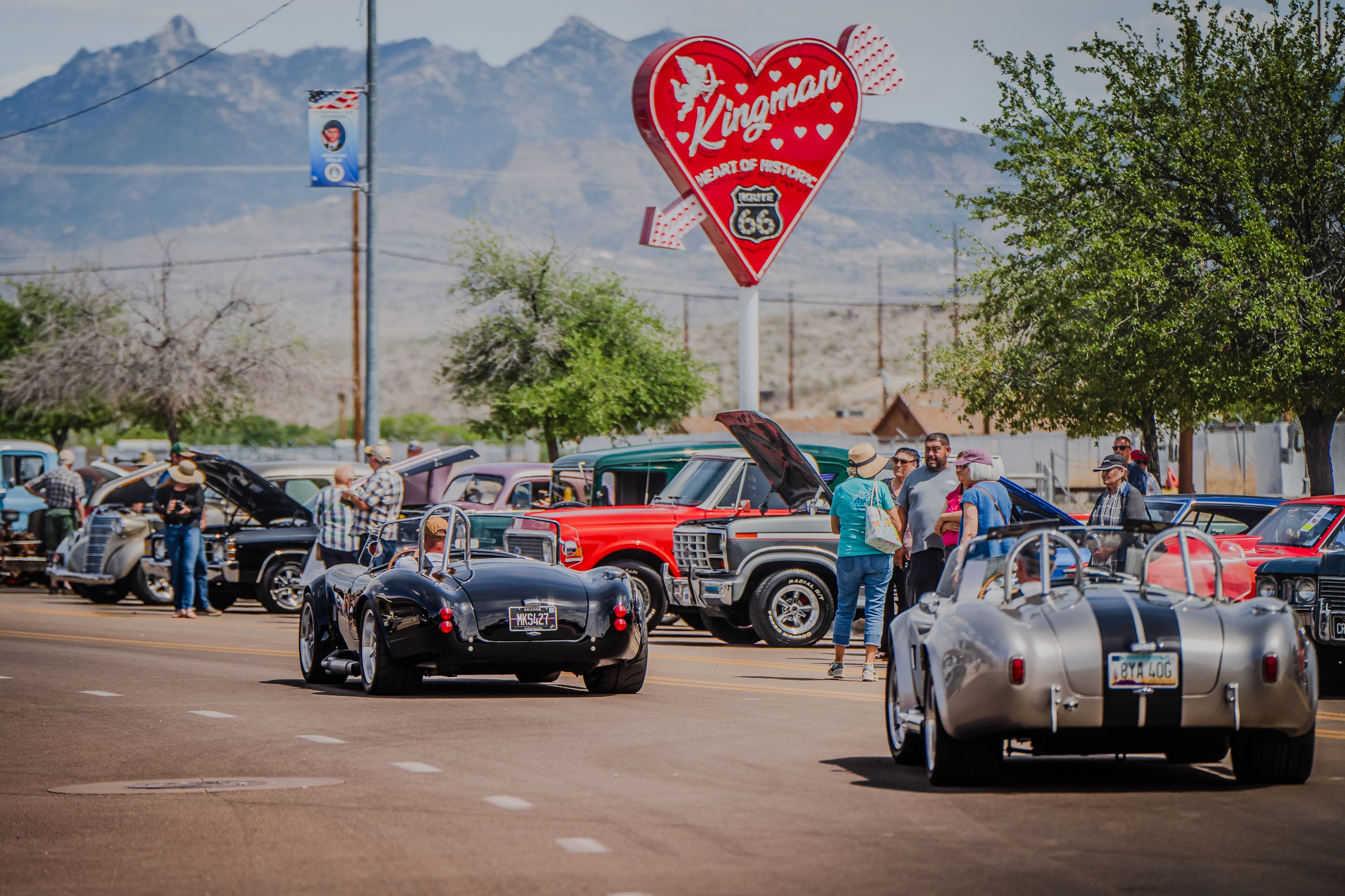 classic cars line the street in Kingman. Mountains in the background and a heart shaped neon sign read "Kingman Heart of Historic Route 66"