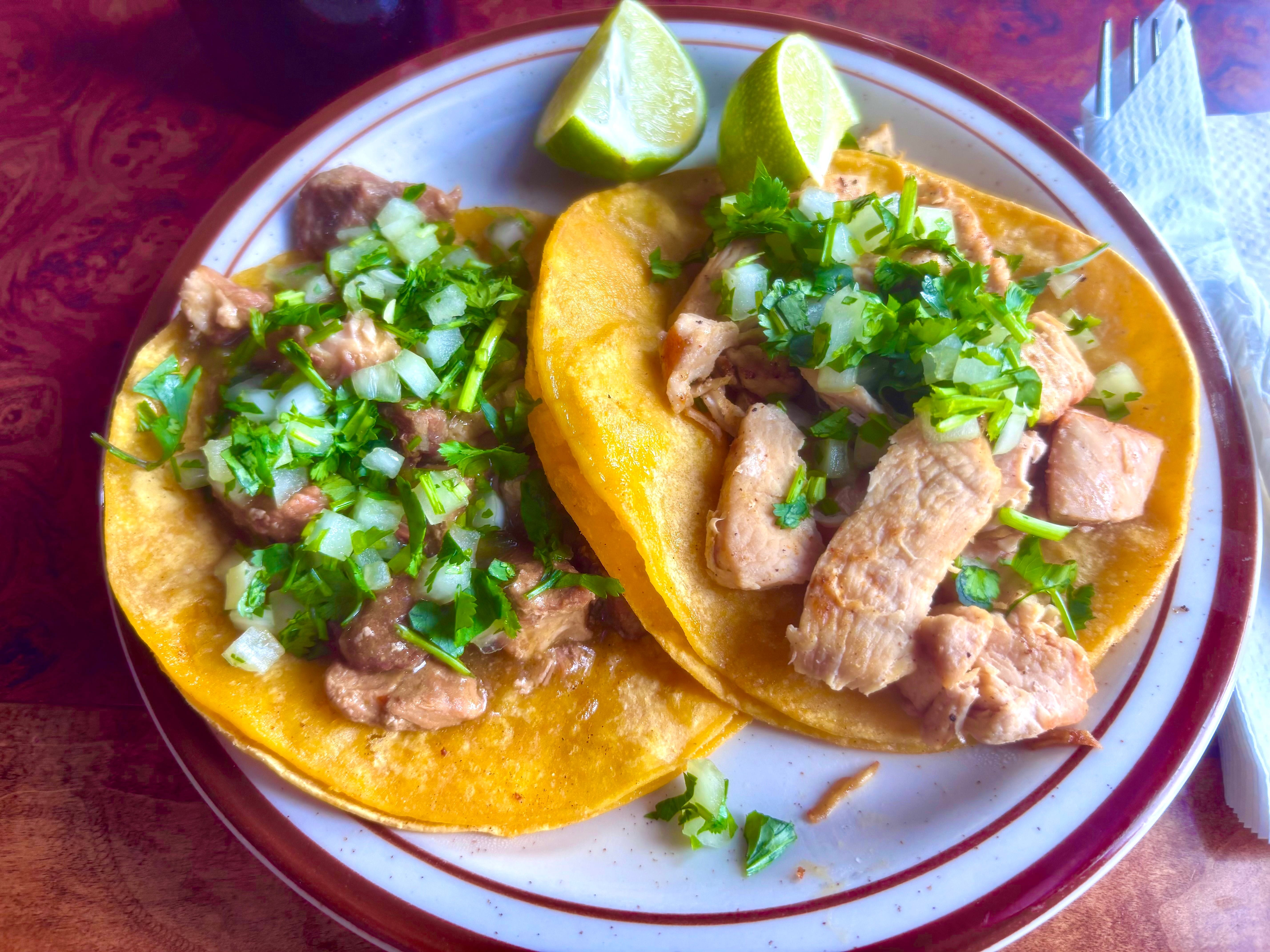 pork tacos on a plate with two lime wedges on the side.