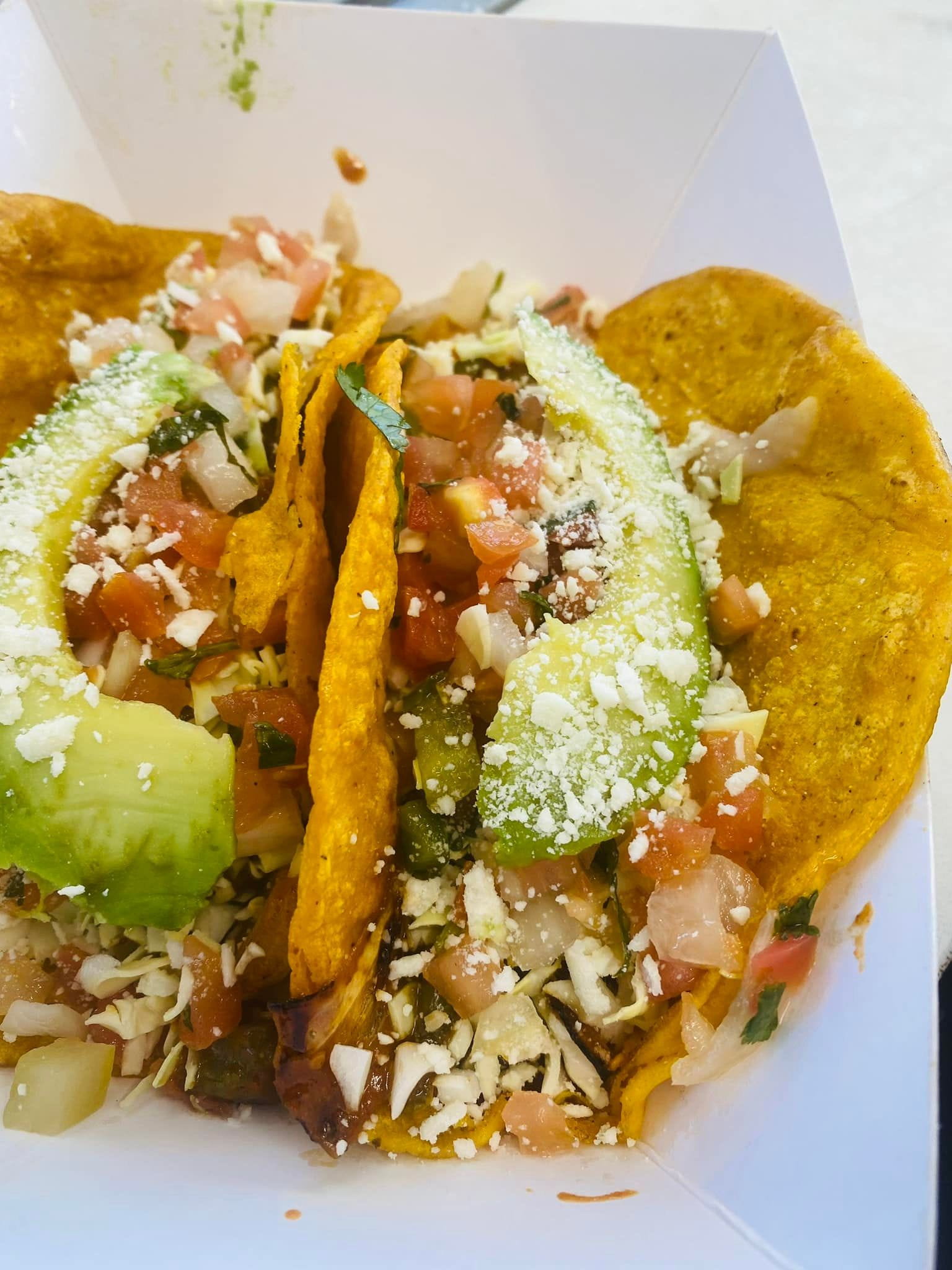 Two tacos on a plate with avocado slices on top.